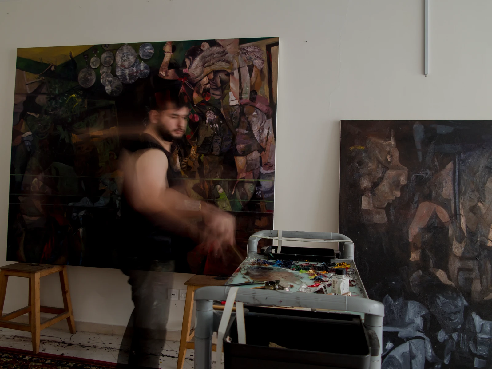The artist in the studio between paintings and a table of paints